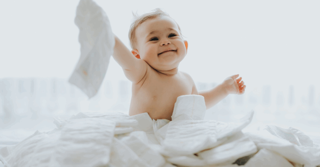 A baby sits happily on a colorful pile of diapers, surrounded by soft fabric and playful patterns.