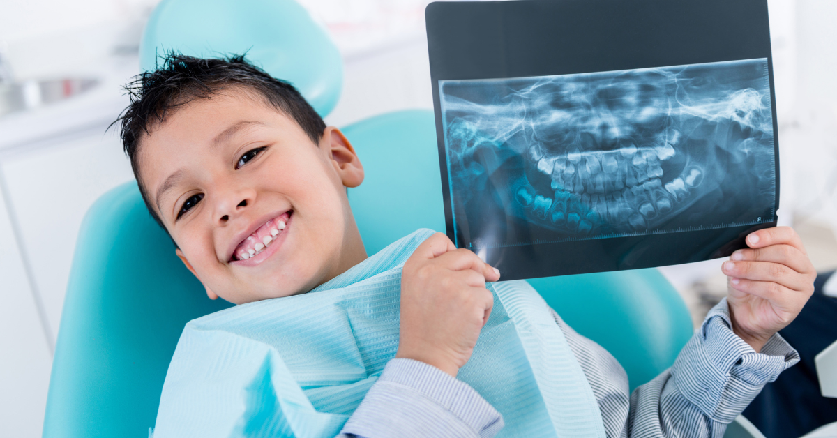 Smiling child in a dental chair holding a dental X-ray. The background is a bright dental office, conveying a cheerful and comfortable atmosphere.