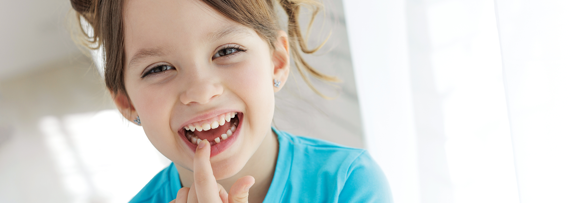 Young girl smiling and pointing to her lost tooth